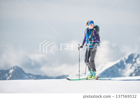 Woman ski mountaineer reaching snowy summit in alpine mountains 137569532
