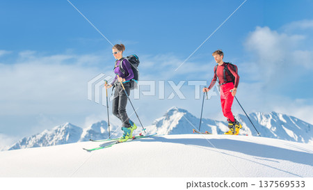 Two ski tourers climbing snowy summit in alpine backcountry Two ski tourers climbing snowy summit in alpine backcountry 137569533