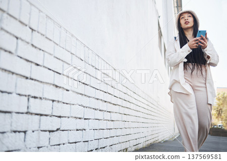 Woman on street with phone, brick wall and walking in city for travel holiday blog on social media. Influencer, streamer or gen z girl on sidewalk with urban fashion, smartphone and content creation Woman on street with phone, brick wall and walking in city for travel holiday blog on social media. Influencer, streamer or gen z girl on sidewalk with urban fashion, smartphone and content creation 137569581