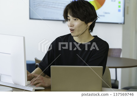 A young Japanese man in casual clothes is surprised while working on a computer in the office 137569746