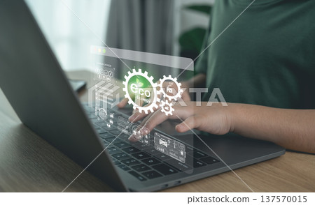 Person typing on laptop with virtual eco ecology and green energy sustainability icons overlay. 137570015