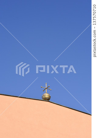 Golden Metal Cross Ornament on Building Roof Against Blue Sky 137570710
