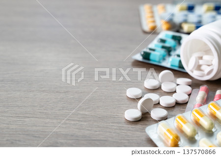 Concept of daily medication routine and chronic disease management. White tablets spilling from bottle with blister capsules on wooden table, symbol of prescription compliance and dosage control at Concept of daily medication routine and chronic disease management. White tablets spilling from bottle with blister capsules on wooden table, symbol of prescription compliance and dosage control at 137570866