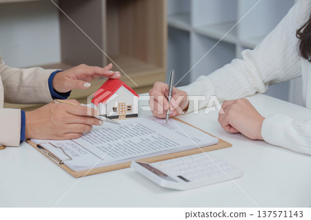 Contract Signing. Client and advisor reviewing home purchase agreement with model house. Contract Signing. Client and advisor reviewing home purchase agreement with model house. 137571143