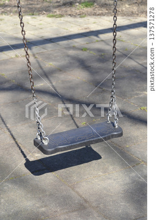 Empty black plastic swing hanging on metal chains in a playground Empty black plastic swing hanging on metal chains in a playground 137571278