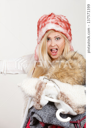 Woman in winter hat holding clothes pile Woman in winter hat holding clothes pile 137571399