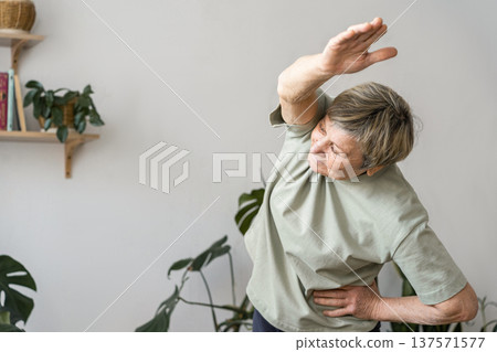 Senior woman doing side bend stretching exercise, keeping fit and healthy at home for her wellbeing and vitality. Mindful happiness, an active, and healthy lifestyle 137571577