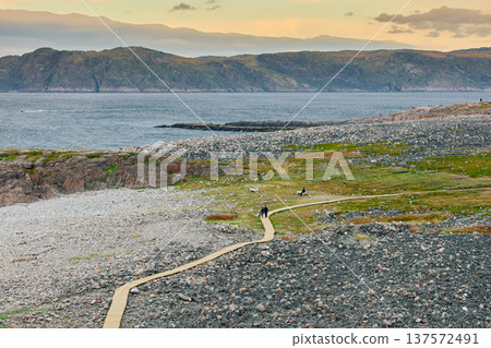 Russia, Teriberka, People walk along a wooden path at sunset, the coast of the Barents Sea, the rocky shore with colourful arctic carpet of moss, yagel, Tundra at autumn, Murmansk Russia, Teriberka, People walk along a wooden path at sunset, the coast of the Barents Sea, the rocky shore with colourful arctic carpet of moss, yagel, Tundra at autumn, Murmansk 137572491