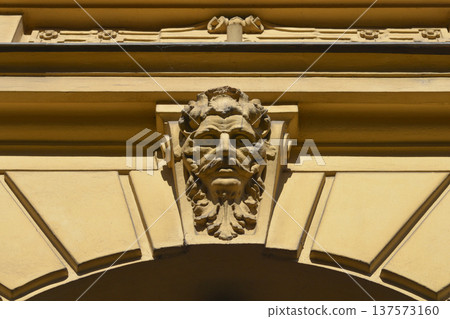 Architectural keystone with a bearded male face relief on a yellow facade Architectural keystone with a bearded male face relief on a yellow facade 137573160