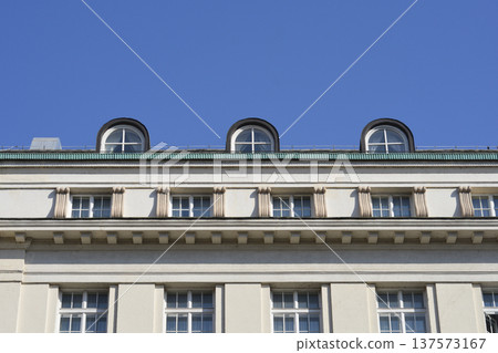 Historical building facade with arched attic windows and blue sky Historical building facade with arched attic windows and blue sky 137573167