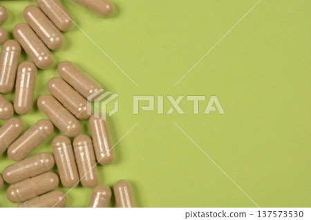 Brown herbal capsules on green background 137573530