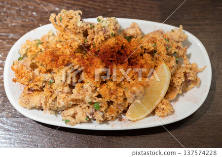 Crispy fried squid tentacles served on a plate with a lemon wedge in a restaurant setting, a golden seafood appetizer with crunchy texture and savory flavor. 137574228