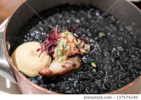Mediterranean squid ink rice served in a metal pan with tender squid and creamy sauce, styled as a rich black seafood dish with elegant restaurant presentation. Mediterranean squid ink rice served in a metal pan with tender squid and creamy sauce, styled as a rich black seafood dish with elegant restaurant presentation. 137574240