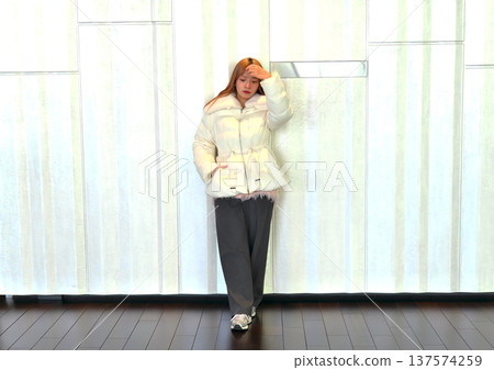 一位女模特兒倚靠在白牆上。這是一張精緻的冬季室內肖像照,她穿著乾淨的白色外套。 一位女模特兒倚靠在白牆上。這是一張精緻的冬季室內肖像照,她穿著乾淨的白色外套。 137574259