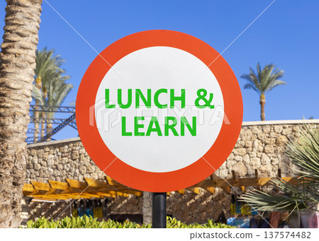 Lunch and learn symbol. Concept words Lunch and learn on beautiful white road sign. Beautiful blue sky palm trees background. Business, educational and lunch and learn concept. Copy space. 137574482