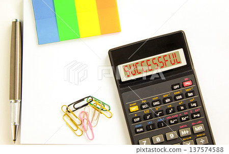 Successful symbol. Concept word Successful on beautiful black calculator's screen. Beautiful white background. Colored paper and black pen. Business successful concept. Copy space. 137574588