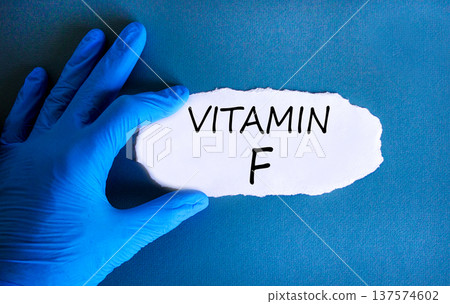 Vitamin F symbol. Concept words Vitamin F on beautiful white paper. Doctor's hand in blue medical glove. Beautiful blue background. Medical healthy lifestyle Vitamin F concept. 137574602