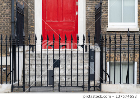 Traditional brick townhouse with a red door and iron fence representing classic British residential architecture in London. Traditional brick townhouse with a red door and iron fence representing classic British residential architecture in London. 137574658