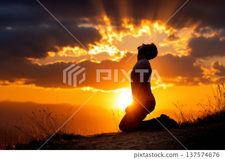 Shepherd Kneels in Prayer on Hilltop at Sunrise With Golden Light in Background Shepherd Kneels in Prayer on Hilltop at Sunrise With Golden Light in Background 137574676