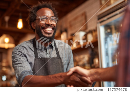Small Black Business Owner Thanks Loyal Customers With Handshake in Cozy Setting During Busy Store Hours 137574678