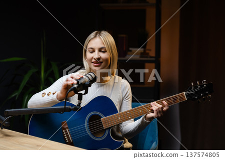 Young woman singing and playing acoustic guitar in recording studio Young woman singing and playing acoustic guitar in recording studio 137574805