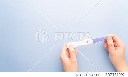 Pregnant woman holding a positive urine pregnancy test on blue background. Pregnancy test kit measure hCG levels in urine. 137574992