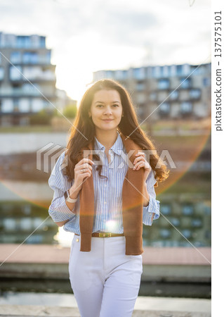 Elegant young woman in old money style walking by riverside near Prague pier during golden hour. Quiet luxury aesthetic and confident European lifestyle concept. Elegant young woman in old money style walking by riverside near Prague pier during golden hour. Quiet luxury aesthetic and confident European lifestyle concept. 137575101