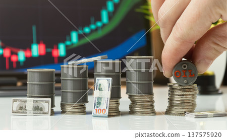 hand placing a miniature oil barrel on stacked coins beside cash and a rising market chart, representing active energy investing. hand placing a miniature oil barrel on stacked coins beside cash and a rising market chart, representing active energy investing. 137575920