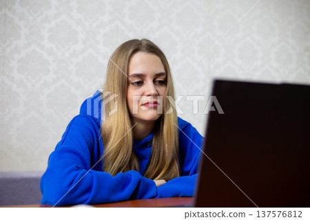 Disappointed blonde girl frowns while watching movie premiere on laptop. She dislikes new film, unimpressed by plot or acting. Negative reaction to online cinema streaming at home 137576812