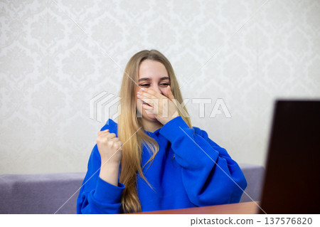 Blonde girl laughs uncontrollably at funny cartoon on laptop, covering mouth with hand. Genuine amusement while watching animated comedy at home. Joyful reaction to humorous content Blonde girl laughs uncontrollably at funny cartoon on laptop, covering mouth with hand. Genuine amusement while watching animated comedy at home. Joyful reaction to humorous content 137576820