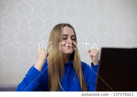 Young blonde woman celebrates university acceptance with clenched fists and closed eyes. Joyful reaction to admission email on laptop. Proud student achieves academic dream at home Young blonde woman celebrates university acceptance with clenched fists and closed eyes. Joyful reaction to admission email on laptop. Proud student achieves academic dream at home 137576821