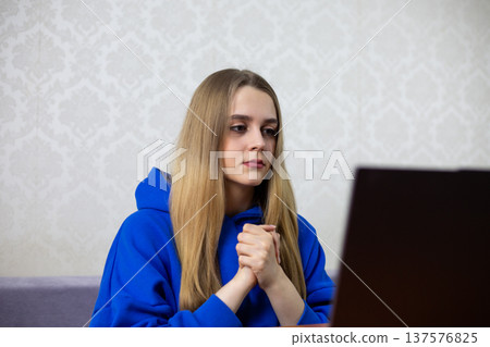 Nervous blonde football fan clasps hands together before penalty kick during live match. Tense moment watching crucial shot on laptop at home. Anxious viewer of broadcast Nervous blonde football fan clasps hands together before penalty kick during live match. Tense moment watching crucial shot on laptop at home. Anxious viewer of broadcast 137576825
