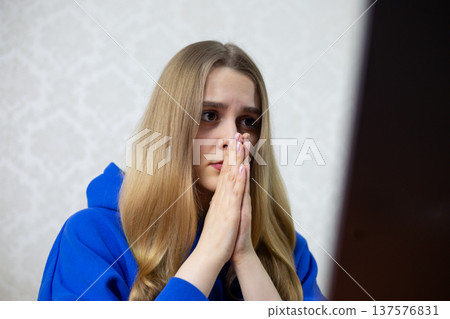 Young woman asks AI chatbot for guidance, hands clasped in digital prayer. She interacts with artificial intelligence on laptop, seeking answers. Futuristic tech concept 137576831