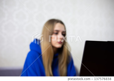 Blurred young woman works on laptop at home, background out of focus. Soft image emphasizes screen and cozy indoor atmosphere. Perfect for technology and lifestyle concepts Blurred young woman works on laptop at home, background out of focus. Soft image emphasizes screen and cozy indoor atmosphere. Perfect for technology and lifestyle concepts 137576838