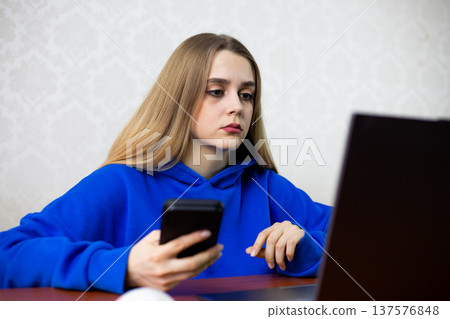 Young woman compares prices on laptop and smartphone while shopping online. She searches for best deal and discount before buying. Consumer behavior and smart shopping concept Young woman compares prices on laptop and smartphone while shopping online. She searches for best deal and discount before buying. Consumer behavior and smart shopping concept 137576848