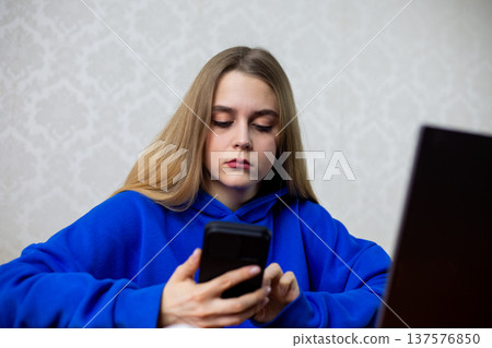 Young woman places sports bet on smartphone while watching live match on laptop. She checks odds and wagers during game broadcast. Online gambling and betting concept at home Young woman places sports bet on smartphone while watching live match on laptop. She checks odds and wagers during game broadcast. Online gambling and betting concept at home 137576850