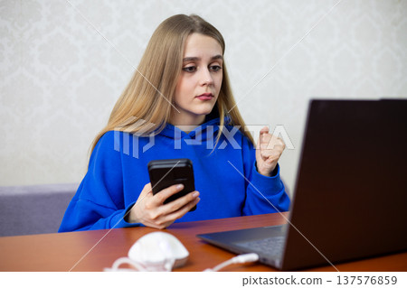 Hopeful young woman awaits loan decision on laptop, fist clenched with tension. She checks banking website anxiously, hoping for financial approval. Credit application concept at home Hopeful young woman awaits loan decision on laptop, fist clenched with tension. She checks banking website anxiously, hoping for financial approval. Credit application concept at home 137576859