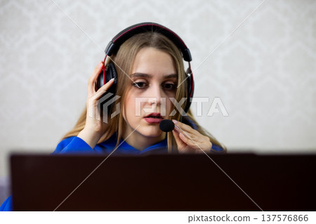 Female streamer adjusts headset microphone while reacting with surprise to online chat. She engages with audience during live broadcast at home studio. Content creator and digital influencer concept Female streamer adjusts headset microphone while reacting with surprise to online chat. She engages with audience during live broadcast at home studio. Content creator and digital influencer concept 137576866