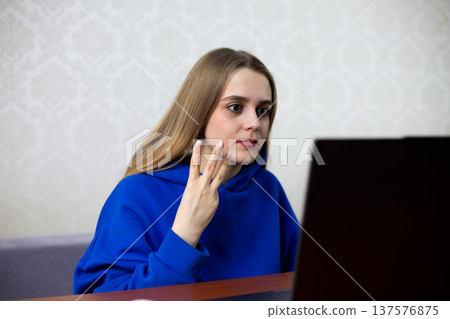 Amazed blonde football fan stares at laptop with wide eyes, raising three fingers. She witnesses incredible hat trick or third goal in match. Stunned reaction to score line at home 137576875