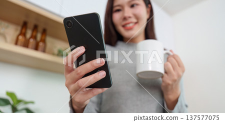 Morning routines. Woman smiling while using smartphone and coffee. 137577075