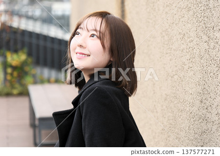 一位女模特兒回頭望向冬日街角。這是一張自然清晰的戶外肖像照，背景是柔和的牆面。 137577271