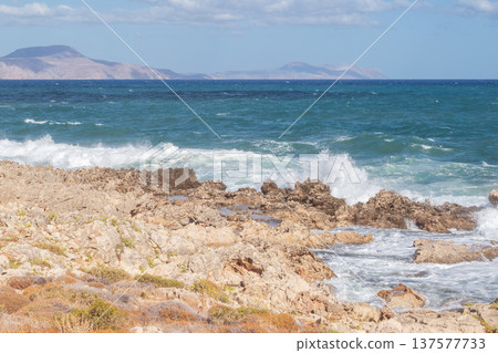 Sea foam crashing against rocky shore. 137577733