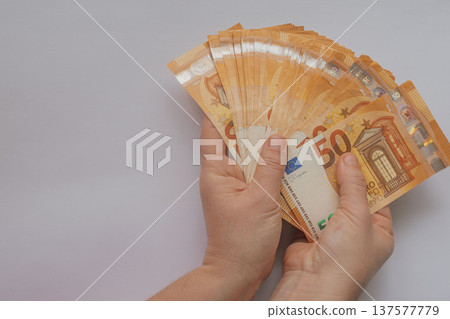 Female hands holding a large fan of 50 Euro banknotes against a white background. High-volume cash concept with orange bills and extensive copy space for design Female hands holding a large fan of 50 Euro banknotes against a white background. High-volume cash concept with orange bills and extensive copy space for design 137577779