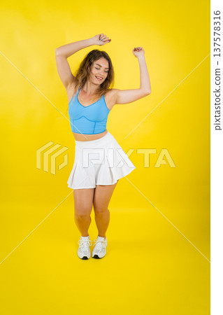 Happy young woman dancing enjoying vibrant yellow background Happy young woman dancing enjoying vibrant yellow background 137578316