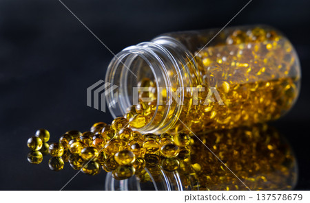 Yellow softgel scattered from transparent jar on greige ston, Nutritional supplements or vitamins Yellow softgel scattered from transparent jar on greige ston, Nutritional supplements or vitamins 137578679