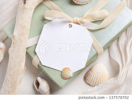 Blank gift tag mockup on sage green present with a ribbon bow near seashells. Summer packaging Blank gift tag mockup on sage green present with a ribbon bow near seashells. Summer packaging 137578702
