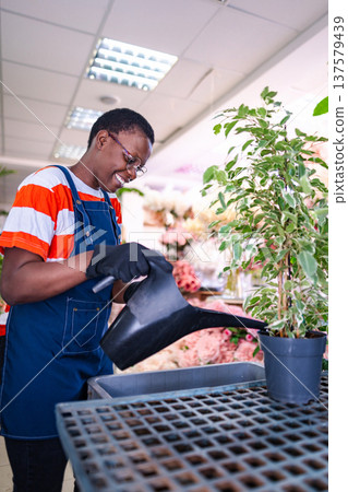 Young florist watering plants in a flower shop Young florist watering plants in a flower shop 137579439