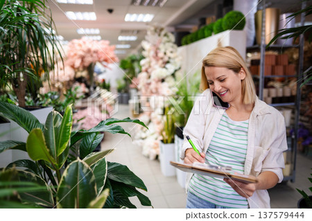 Florist taking notes while speaking on the phone in a flower shop Florist taking notes while speaking on the phone in a flower shop 137579444