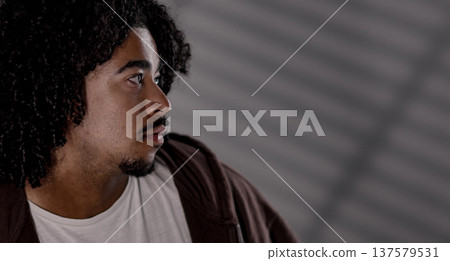 Young african-american man with curly hair looking away from camera with serious expression Young african-american man with curly hair looking away from camera with serious expression 137579531