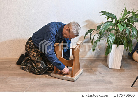 Man fixes wooden chair in a home setting with a plant nearby Man fixes wooden chair in a home setting with a plant nearby 137579600
